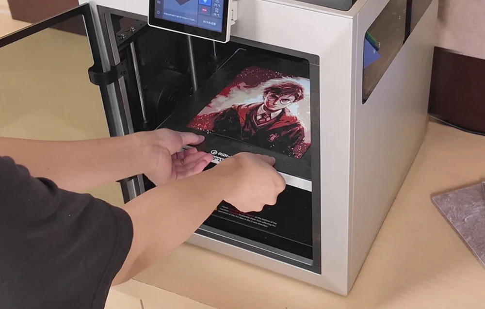 O persoană scoate o imprimare colorată dintr-o imprimantă 3D așezată pe un birou