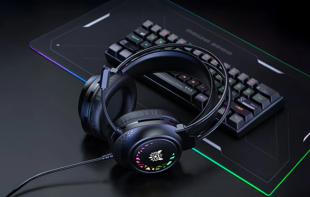 Căști de gaming negre cu retroiluminare colorată sprijinite de o tastatură pe un birou întunecat