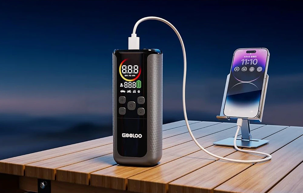 Compresorul portabil GOOLOO încărcând un smartphone prin intermediul unui cablu USB pe o masă de lemn