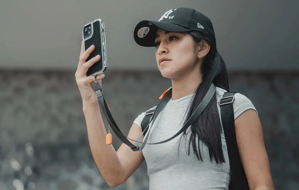 O femeie care poartă o șapcă de baseball își folosește telefonul, care este montat pe o curea de gât gri