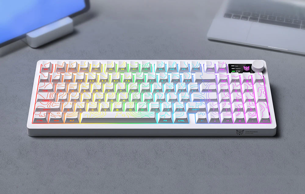 O tastatură cu iluminare colorată se află pe un birou gri lângă o tabletă și un laptop