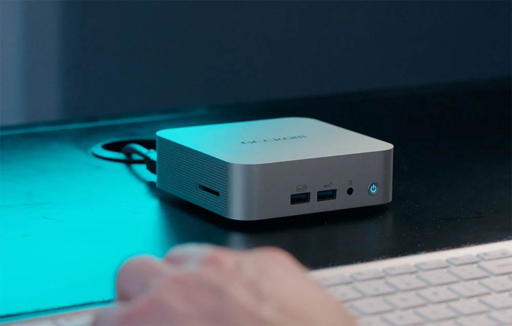 O persoană tastând pe o tastatură albă, cu un mini PC Geekom în fața ei