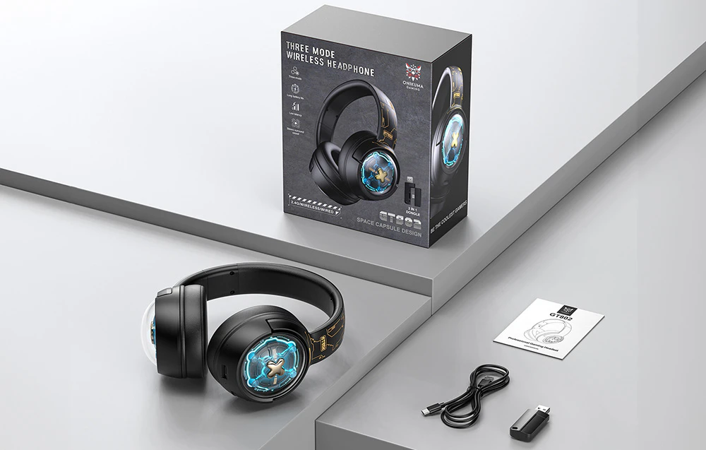 Căști gaming Onikuma așezate pe un birou gri lângă o cutie, manual de utilizare, cablu și adaptor USB