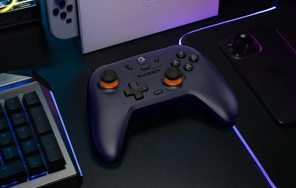 Controler de jocuri negru așezat pe un birou lângă o tastatură, un telefon și o consolă Nintendo Switch