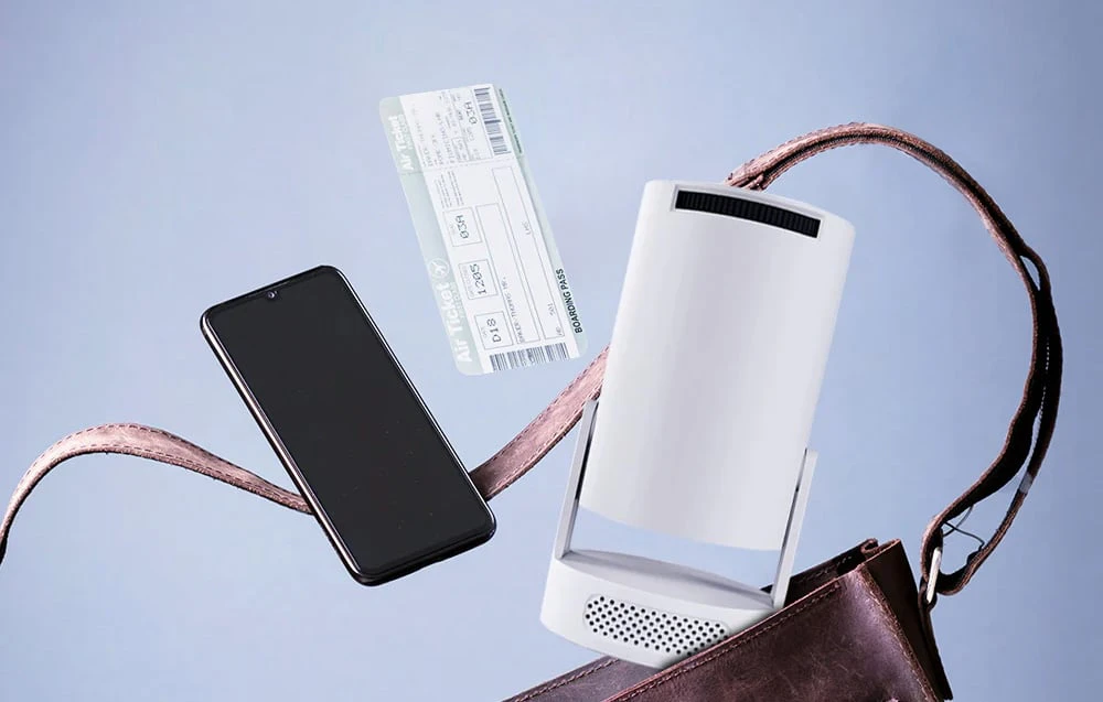 Un proiector alb, un smartphone și un bilet de avion plutesc deasupra unei genți deschise, din piele maro, pe un fundal deschis