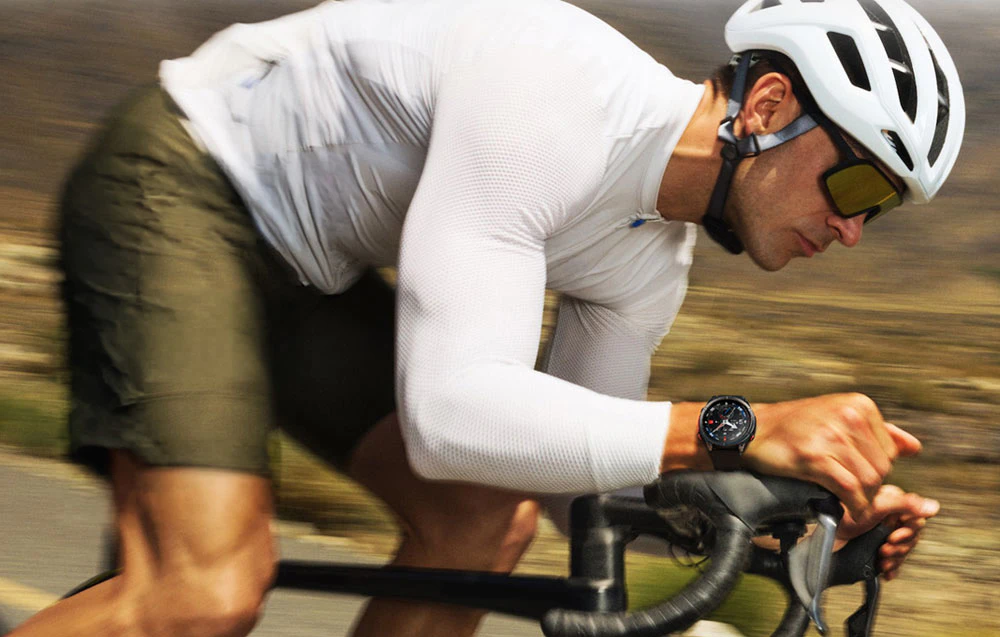 Un ciclist care poartă o cască albă în timp ce merge cu bicicleta, cu un ceas sportiv negru vizibil la încheietura mâinii