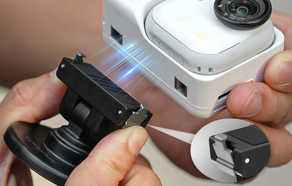 Mâini care atașează un suport magnetic negru la partea inferioară a camerei Insta360 GO 3 albe, cu un prim-plan al clemei.