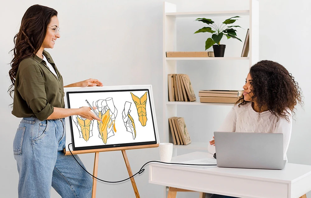 Două femei discutând despre o diagramă anatomică pe un monitor ZEUSLAP așezat pe un șevalet din lemn