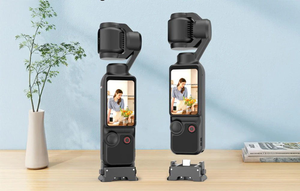 Două camere Osmo Pocket 3 cu adaptoare Puluz montate stau pe o masă de lemn lângă o vază cu o floare