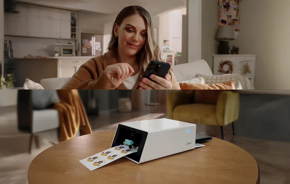 O femeie își folosește smartphone-ul pentru a transfera wireless fotografii către o imprimantă Liene așezată pe o măsuță de cafea.