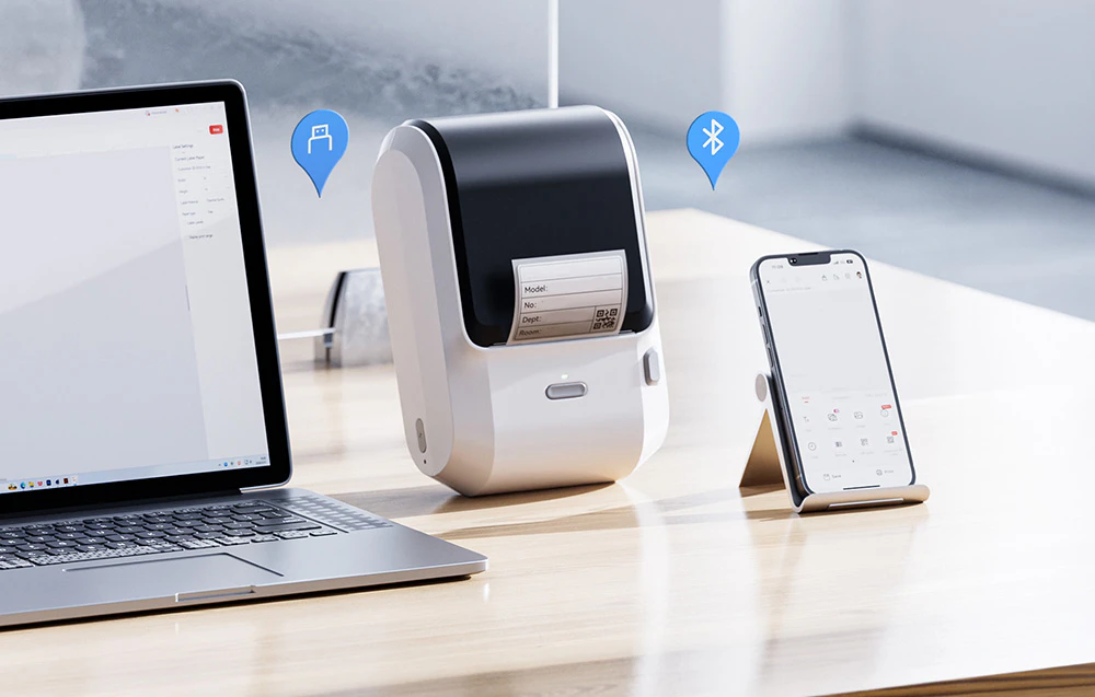 Imprimantă portabilă de etichete conectată prin Bluetooth la un smartphone și prin cablu USB la un laptop