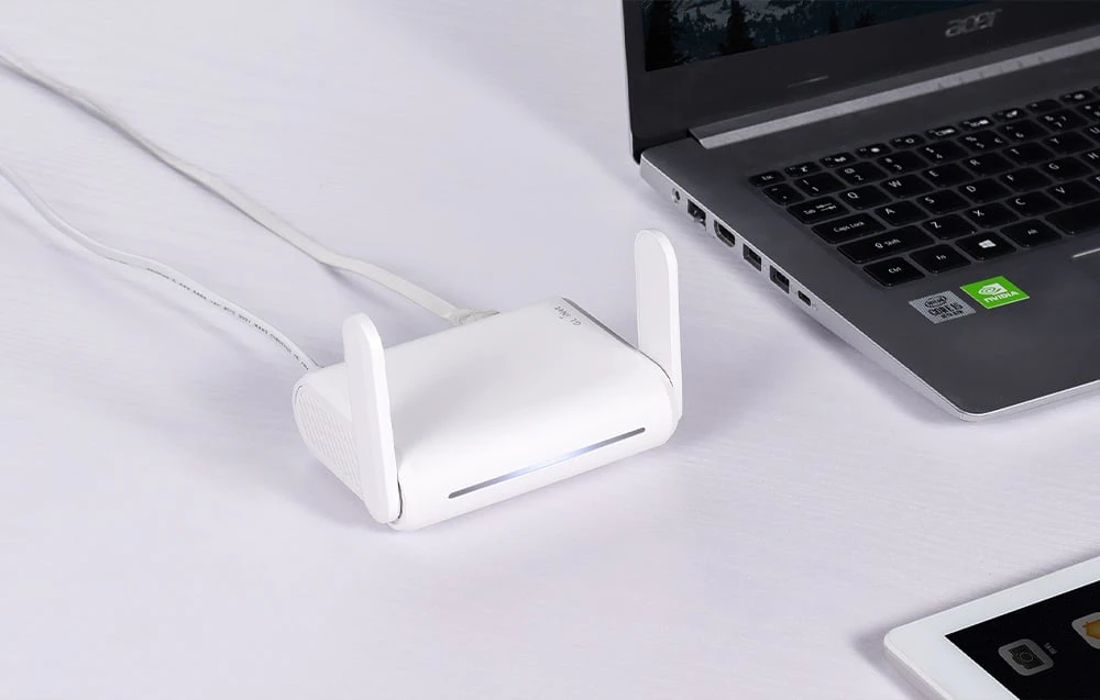 Un router alb așezat pe un birou lângă un laptop și o tabletă