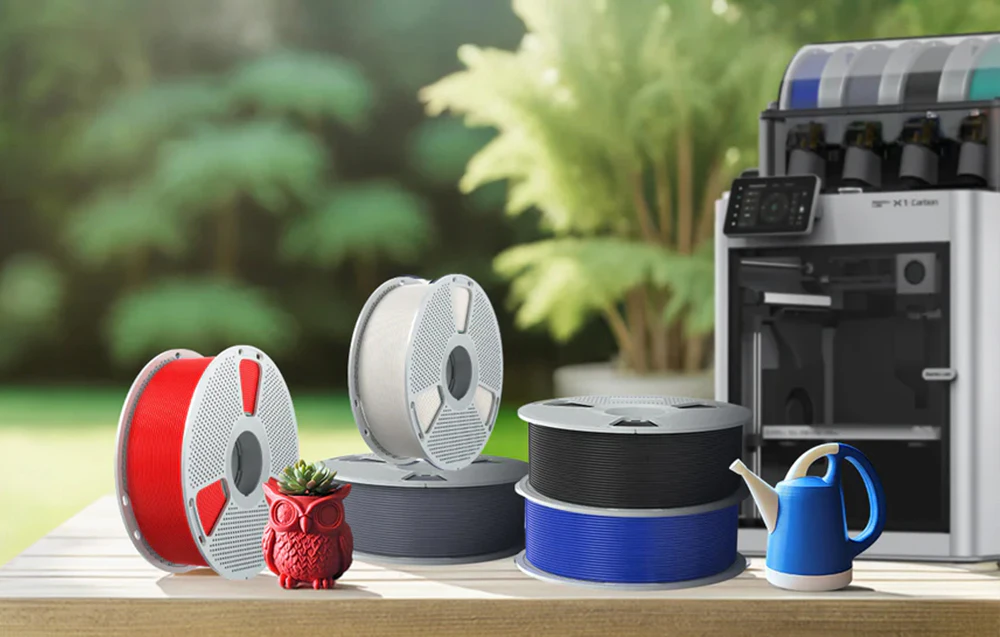 Bobine de filament SUNLU ASA în diverse culori așezate lângă o imprimantă 3D pe o masă în grădină