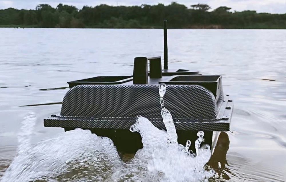Barca de momeli din carbon din spate cu fântână de apă pe lac, containere goale și antena de deasupra vizibile