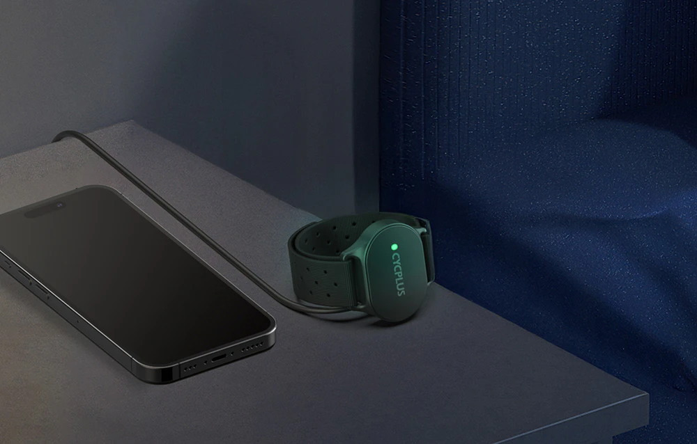 Brățară Cycplus H1 verde cu lumină LED verde lângă smartphone pe suprafață întunecată