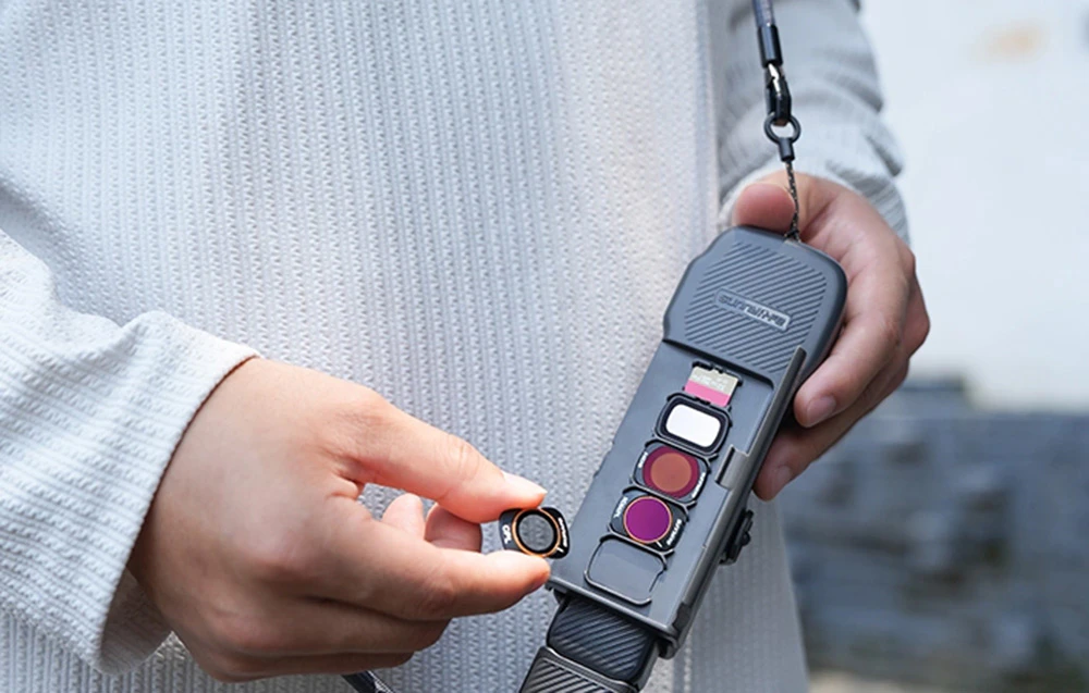 Persoană care ține în mână o husă gri închis cu clapetă deschisă, prezentând filtre și card microSD