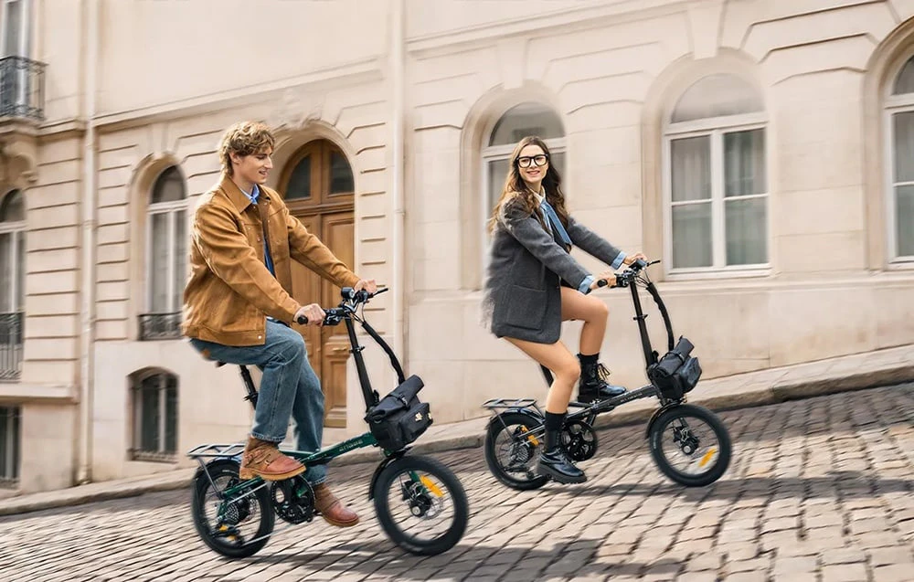 O femeie și un bărbat merg cu biciclete electrice pliabile pe o stradă pietruită din centrul orașului