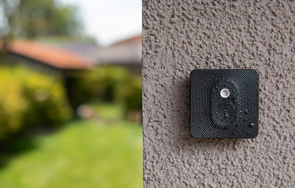 Un buton Shelly negru acoperit de picături de apă, montat pe un perete exterior brut