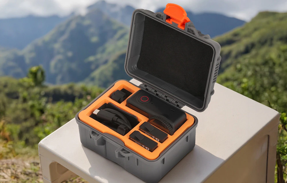 Geantă de protecție Sunnylife deschisă cu accesorii pentru camera foto, așezată pe o masă în aer liber, cu munții în fundal