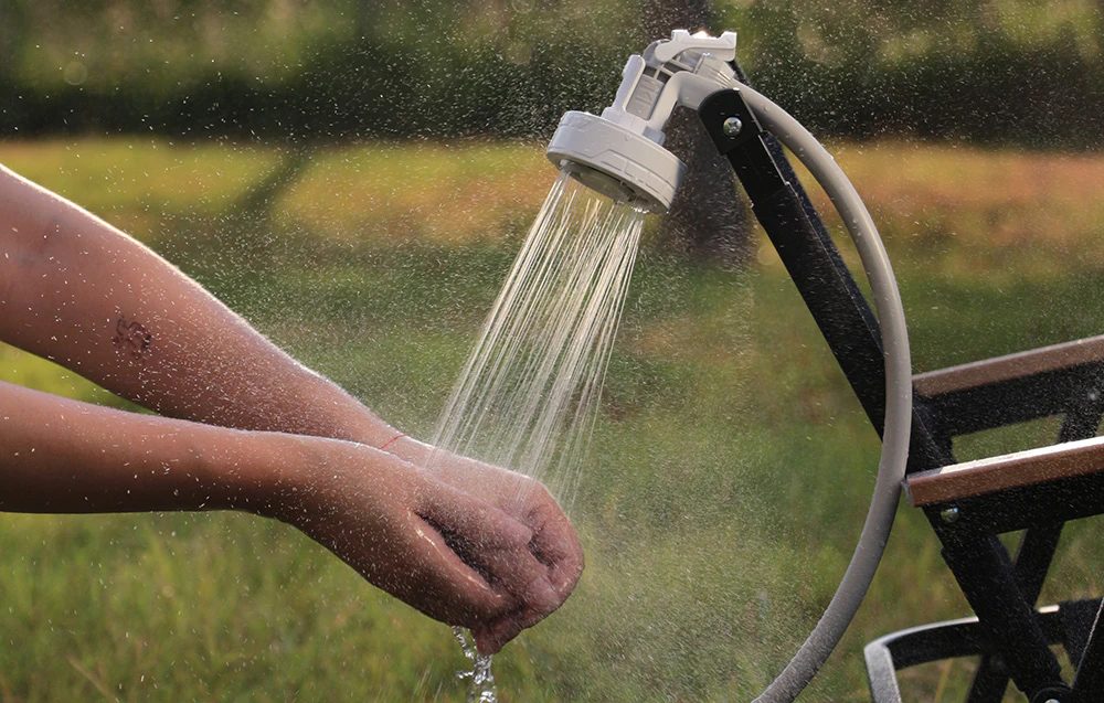 Dușul portabil Flextail Max Shower montat pe o bancă în timp ce se spală mâinile în aer liber.