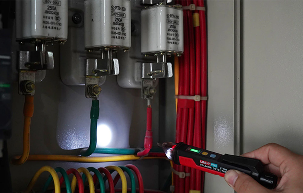 O mână cu un senzor de tensiune care luminează firele din interiorul unei cutii electrice cu siguranțe mari.