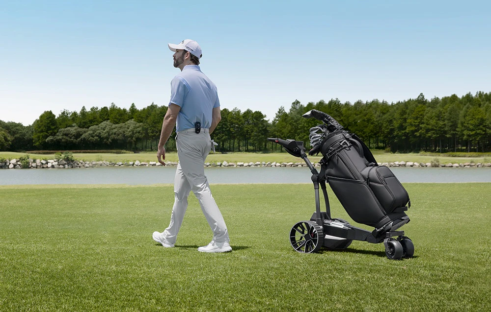Un jucător de golf traversează terenul de golf lângă un cărucior electric cu un sac de golf lângă lac