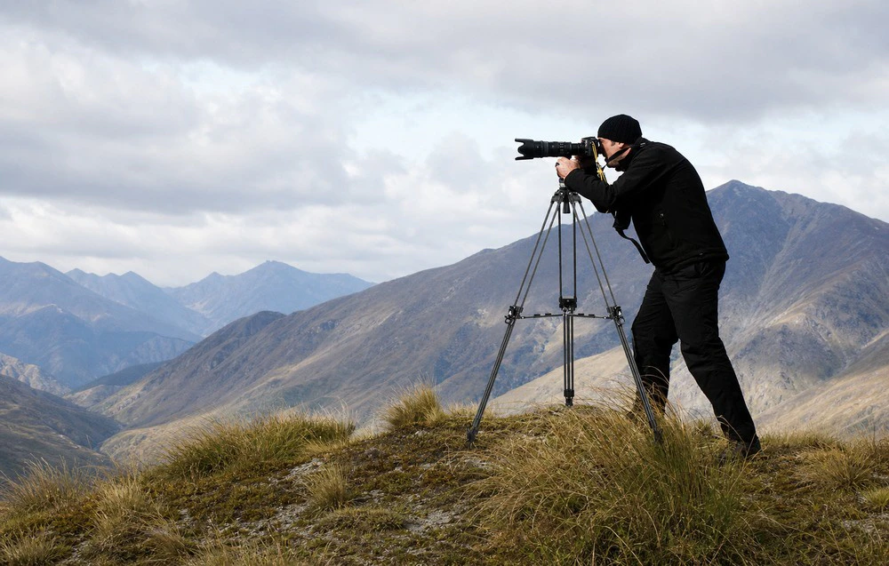 Fotograf care face o fotografie cu un aparat foto pe un trepied într-un peisaj montan