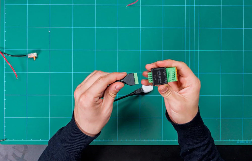Mâini pregătindu-se să conecteze conectorul firului verde în priza de pe modulul ADDON SSR pe un covoraș verde