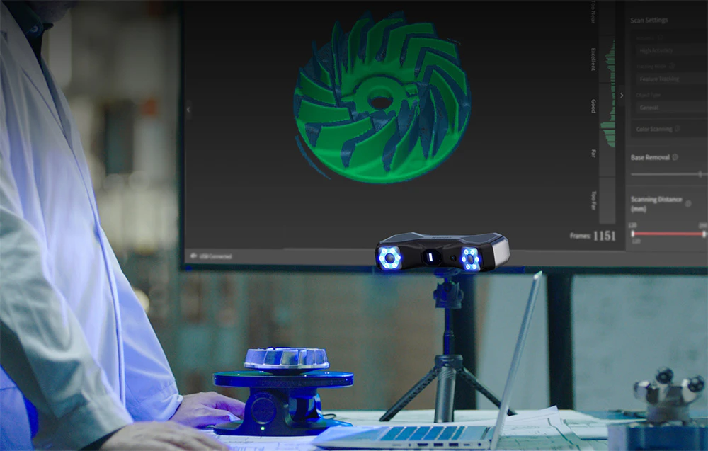 O persoană stă în fața unui birou cu un monitor și un scaner pe un trepied, scanând un produs