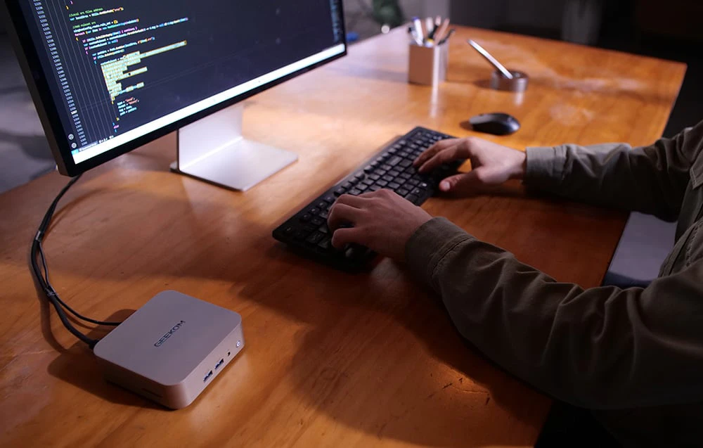 O persoană care lucrează la un birou cu un mini PC, monitor, tastatură și mouse
