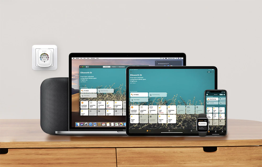 O priză inteligentă montată pe perete lângă un set de dispozitive Apple, inclusiv un laptop, o tabletă, un smartphone, un ceas și o boxă care rulează o aplicație de control al locuinței
