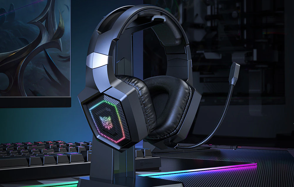 Căști de gaming Onikuma agățate de un suport, monitorul și tastatura pot fi văzute în fundal