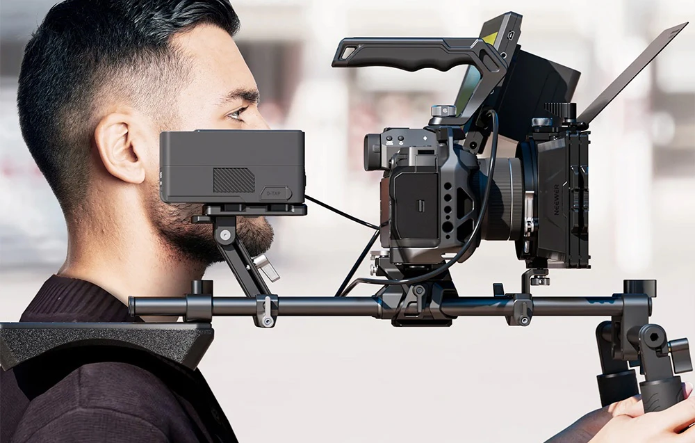Profilul unui operator într-un suport de umăr care transportă un kit de filmare cu o cameră, monitoare și o carcasă pe umăr.