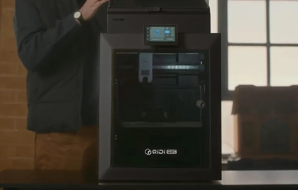 Imprimantă 3D neagră cu o persoană în picioare în fundal