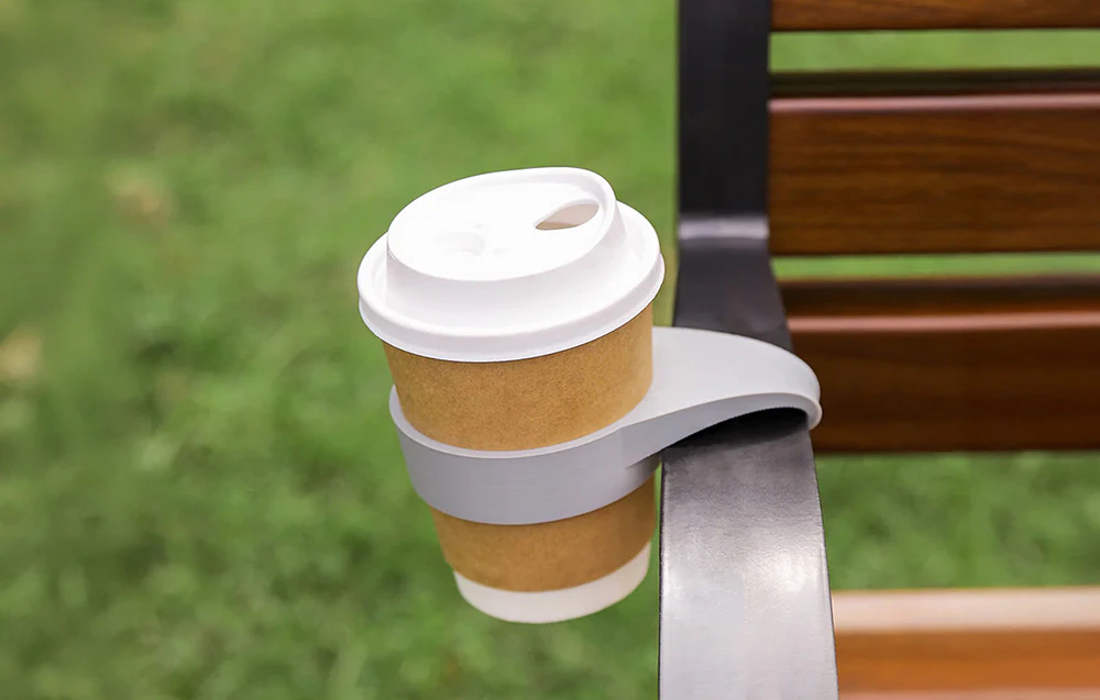 Un suport pentru ceașcă de cafea atașat la brațul unei bănci din parc