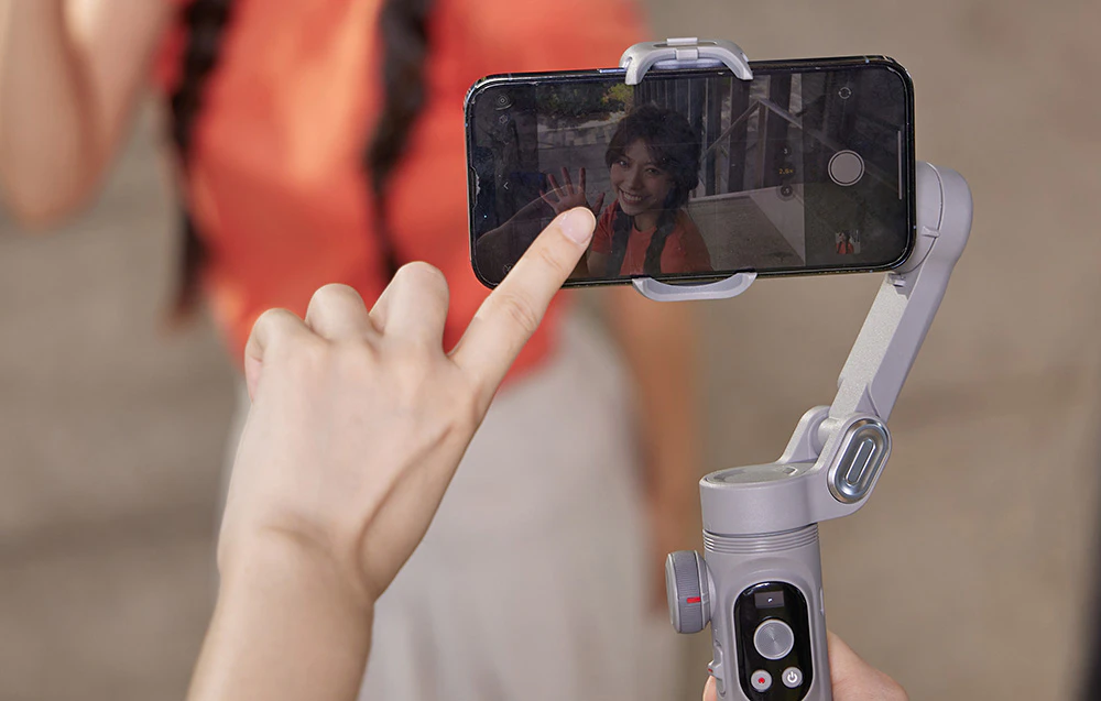 Un smartphone montat pe un gimbal înregistrează un selfie, iar utilizatorul atinge ecranul pentru a regla focalizarea.