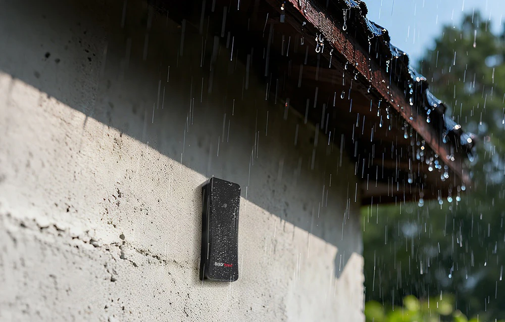 Un senzor exterior negru pentru stația meteorologică Baldr Therm montat pe fațada clădirii în timpul ploii