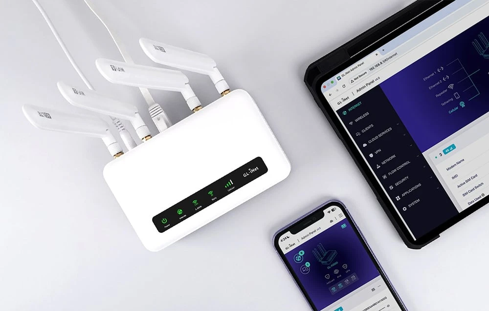 Un router alb cu antenele extinse, așezat lângă un smartphone și o tabletă pe care se afișează panoul de administrare.