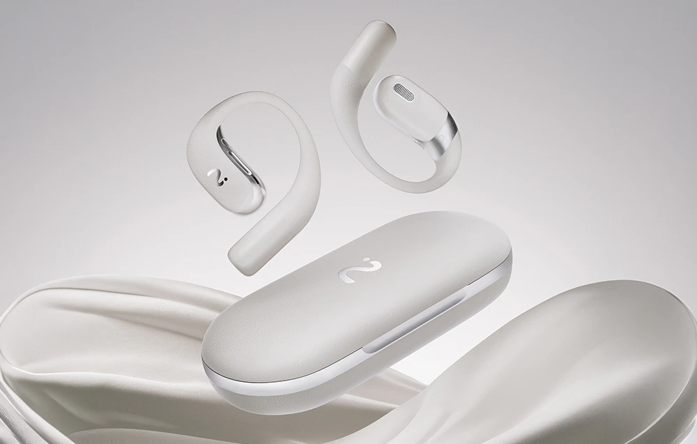 Căști wireless albe plutind deasupra unei carcase albe închise, așezate pe o țesătură de culoare deschisă, șifonată.