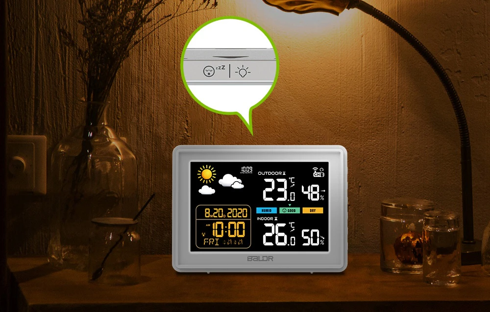 Stația meteorologică Baldr așezată pe o noptieră într-un dormitor cu iluminare ambientală. Deasupra dispozitivului se vede un prim-plan al butonului superior cu pictogramele de amânare a alarmei și de iluminare de fundal