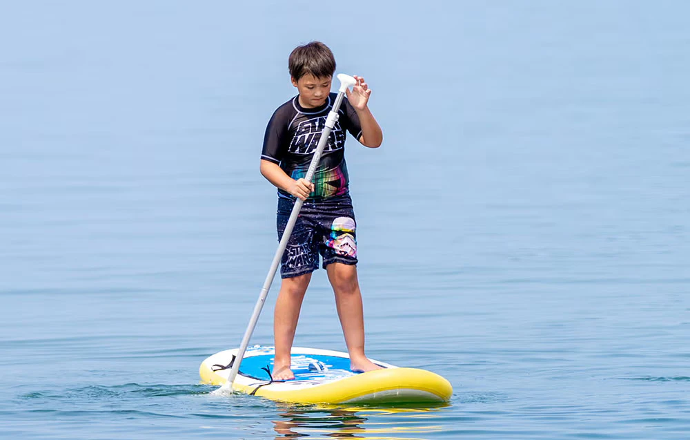 Băiat pe o placă de surf cu o vâslă în mână