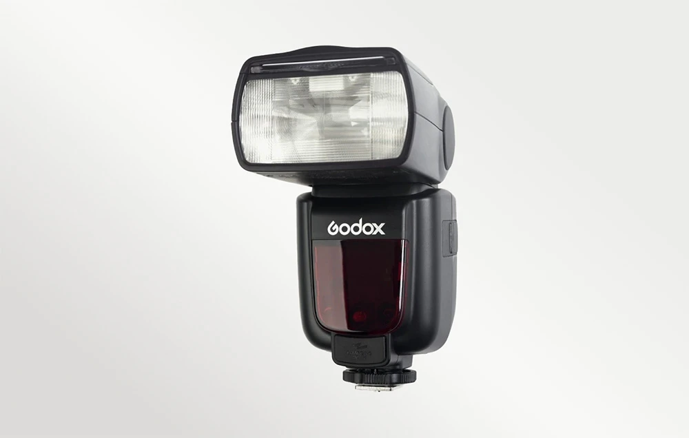 Bliț Godox negru cu un reflector luminos și un element frontal roșu pe un fundal deschis