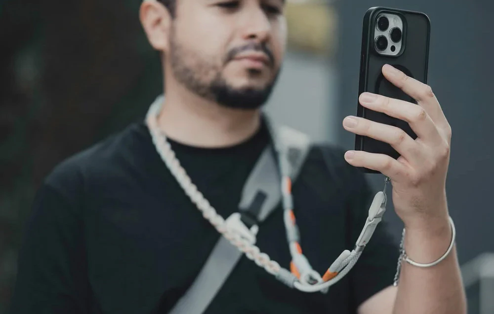 Un bărbat în tricou negru utilizează un smartphone montat pe o curea de gât PGYTECH
