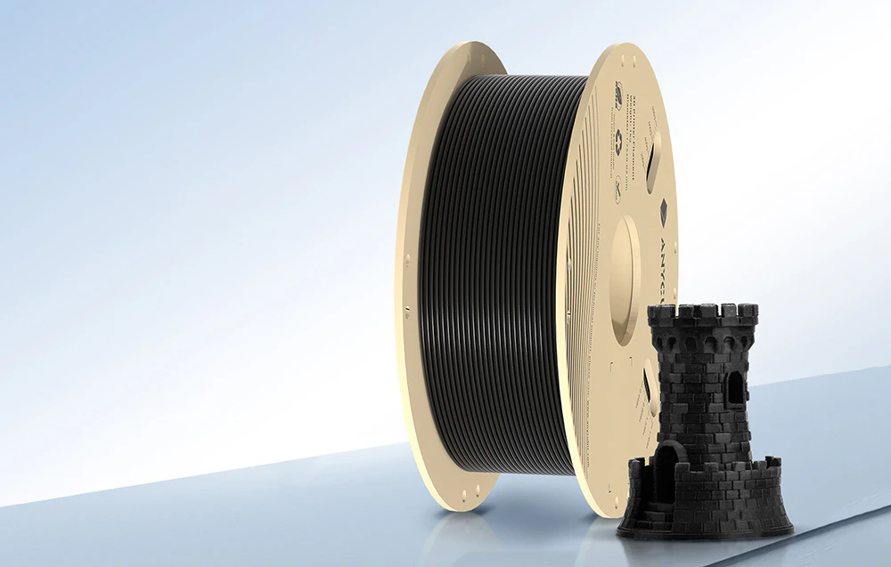 O bobină mare de filament negru pentru imprimanta 3D se află lângă modelul imprimat negru al turnului castelului