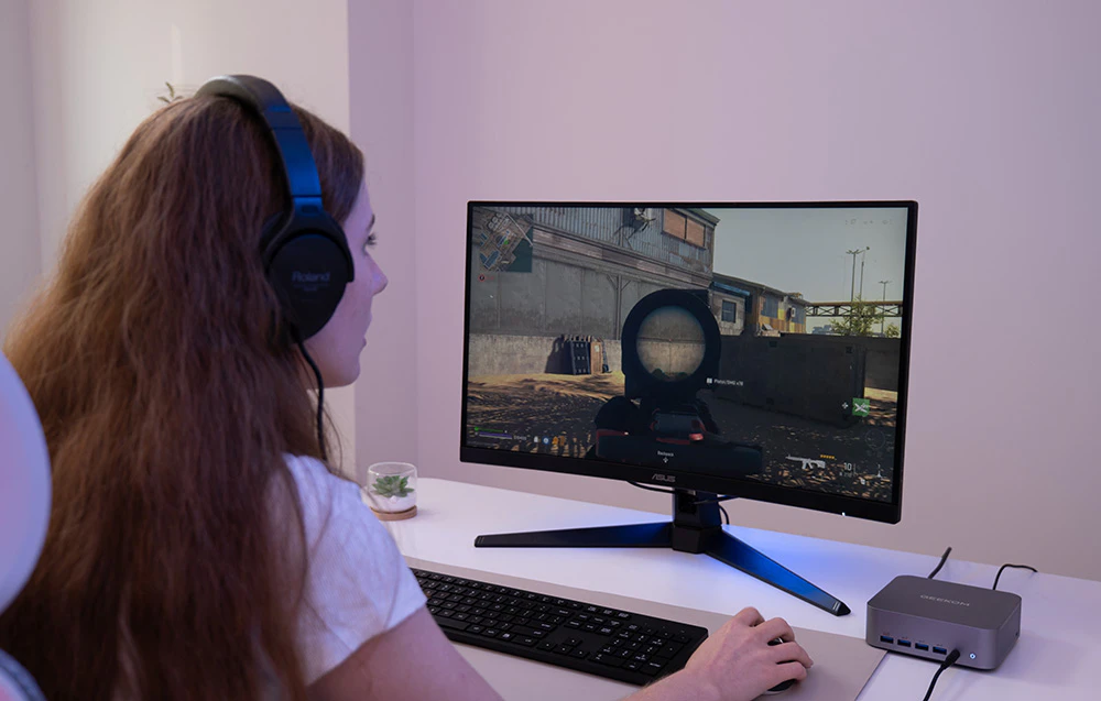 O femeie stă la un birou cu căști pe urechi și joacă un joc pe computer