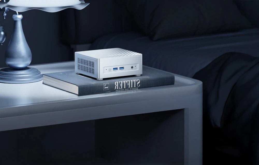 mini PC alb pe o masă, pe o carte, lângă o lampă de podea