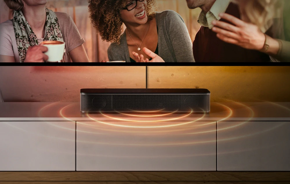 Un soundbar negru pe o comodă albă sub televizor