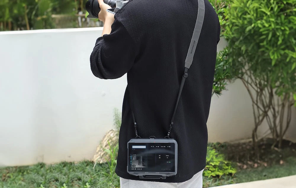 O persoană într-un hanorac negru cu telecomanda pentru dronă agățată de o curea purtată pe umăr