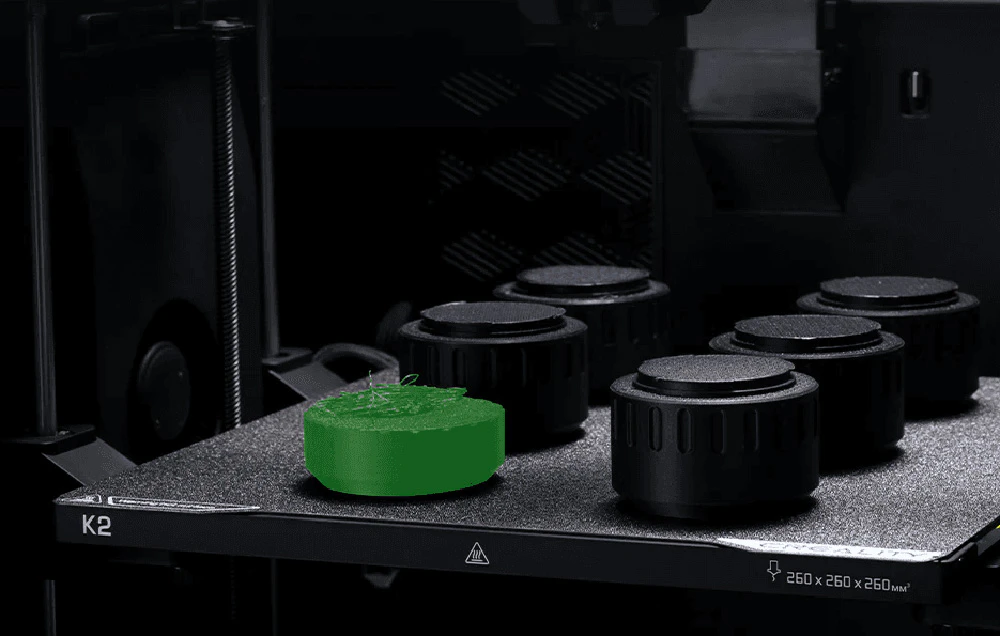 Imprimantă 3D cu model verde pe platforma de imprimare lângă butoane negre