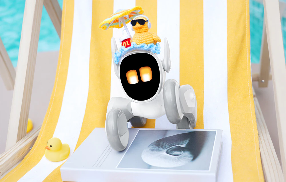 Robotul interactiv Loona, îmbrăcat într-un costum cu model de rață, stă așezat pe un șezlong alb și galben, cu un pui de rață galben în stânga
